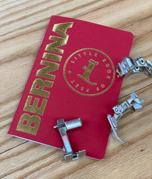 Red 'Bernina' book with sewing machine presser feet on a wooden surface Red 'Bernina' book with sewing machine presser feet on a wooden surface