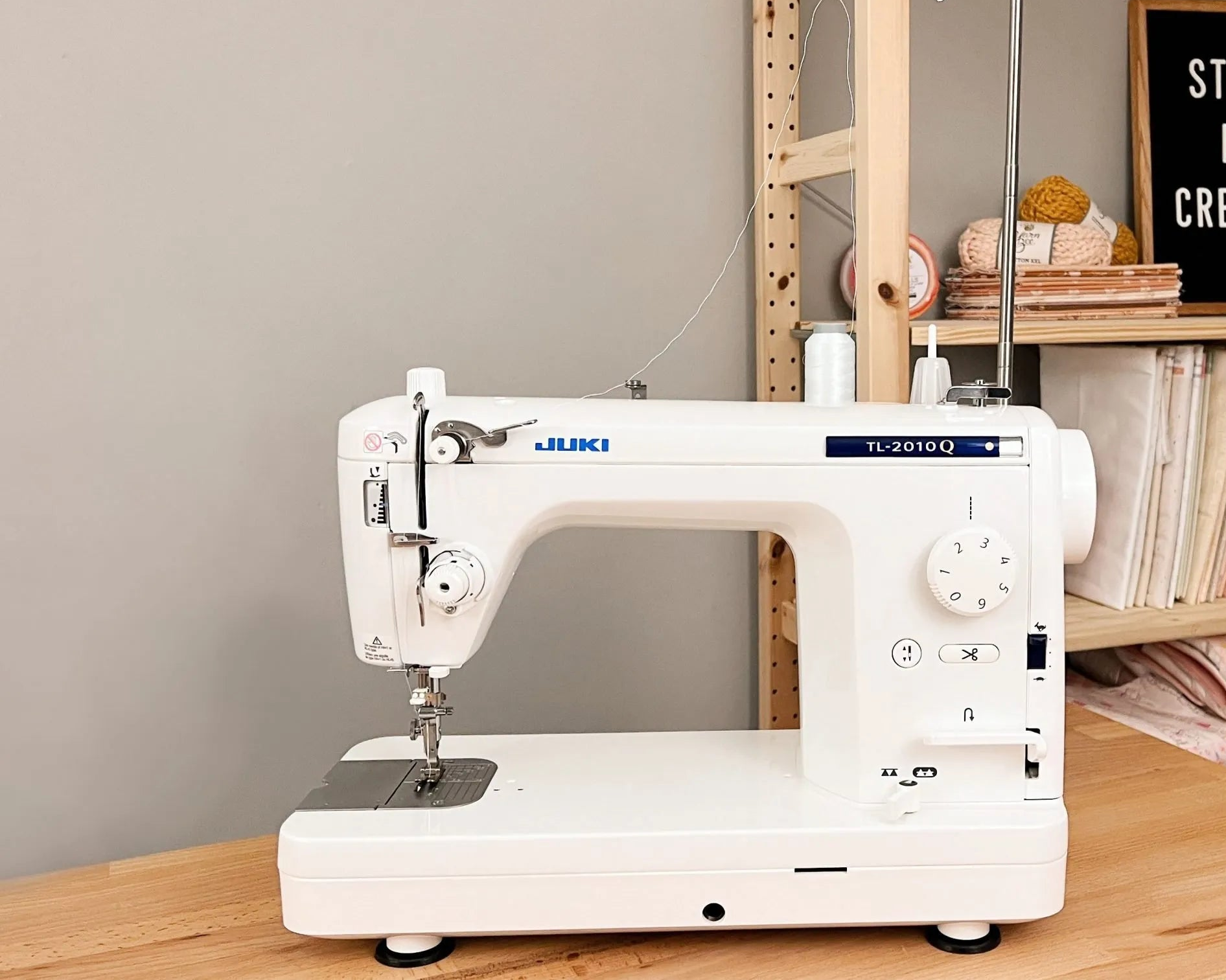 White sewing machine on a wooden table with a bookshelf in the background