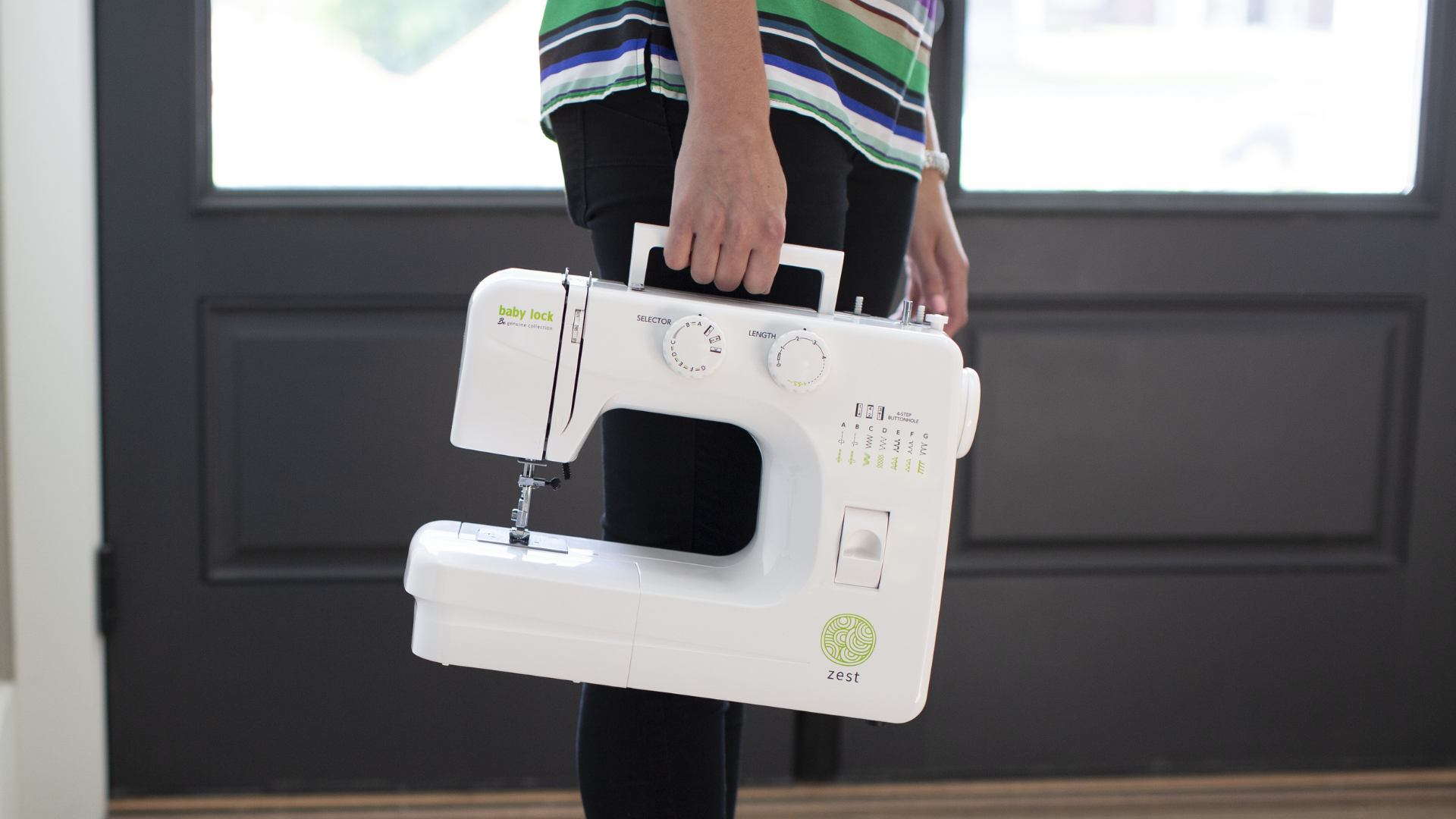 Person holding a Baby Lock Zest sewing machine in front of a dark door
